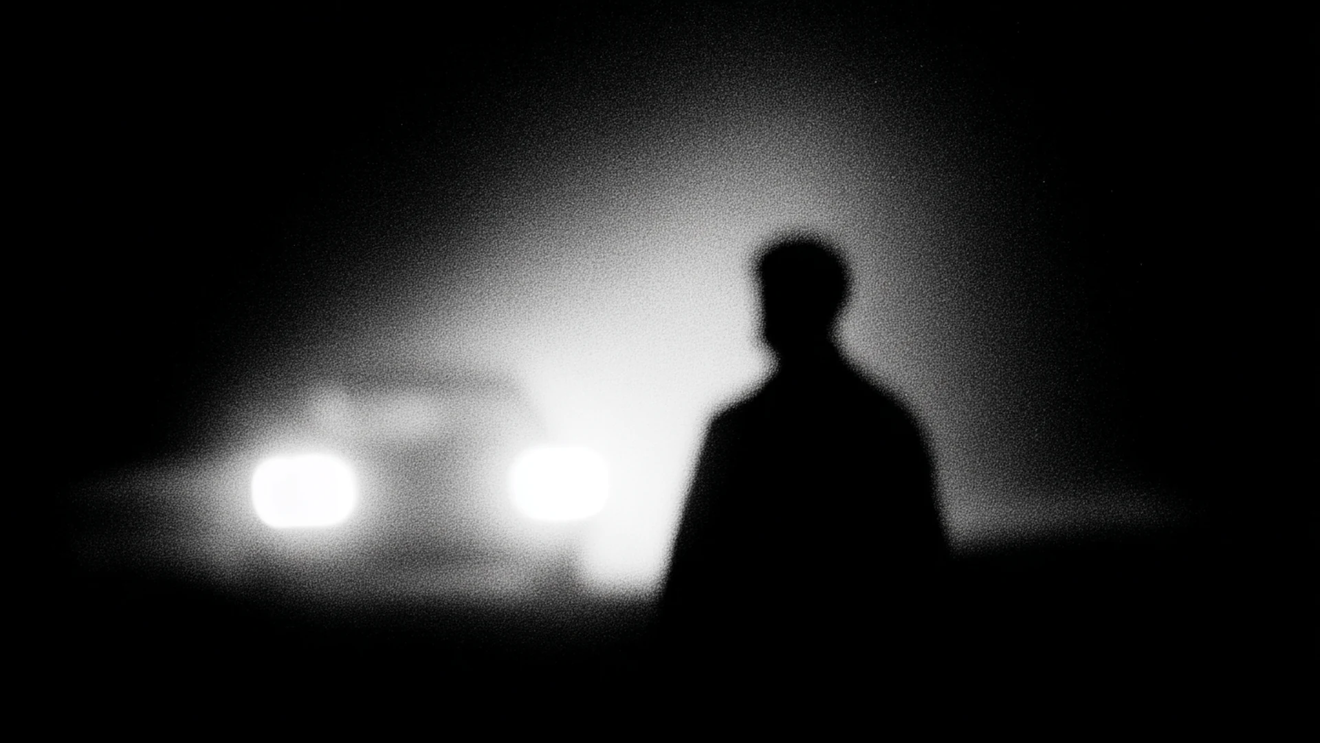 A person silhouetted against approaching headlights.