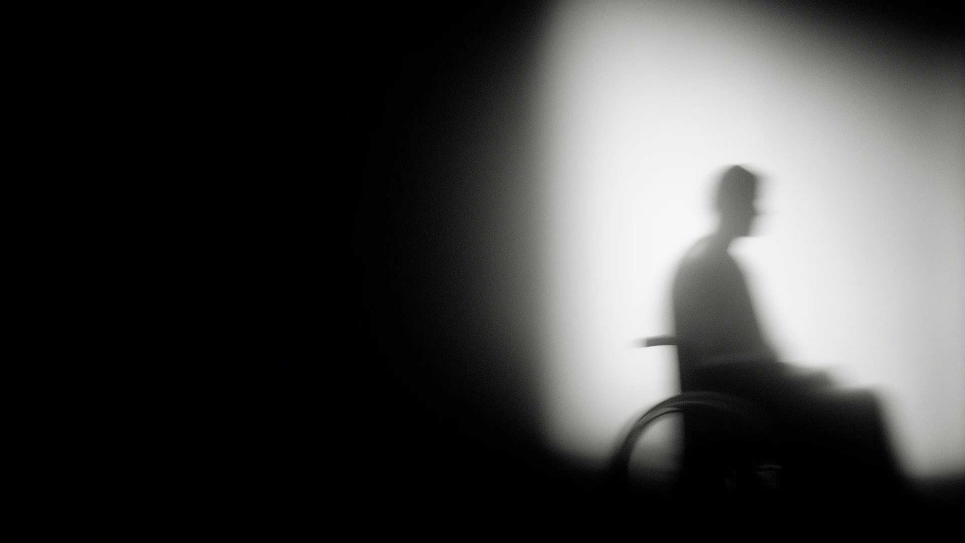 A person in a wheelchair, seen in silhouette against a bright window.